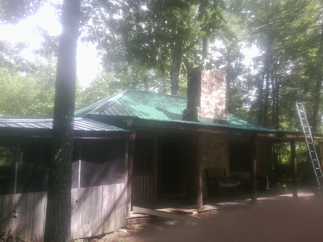 Green metal roof and stone chimney above a log cabin porch in Milton